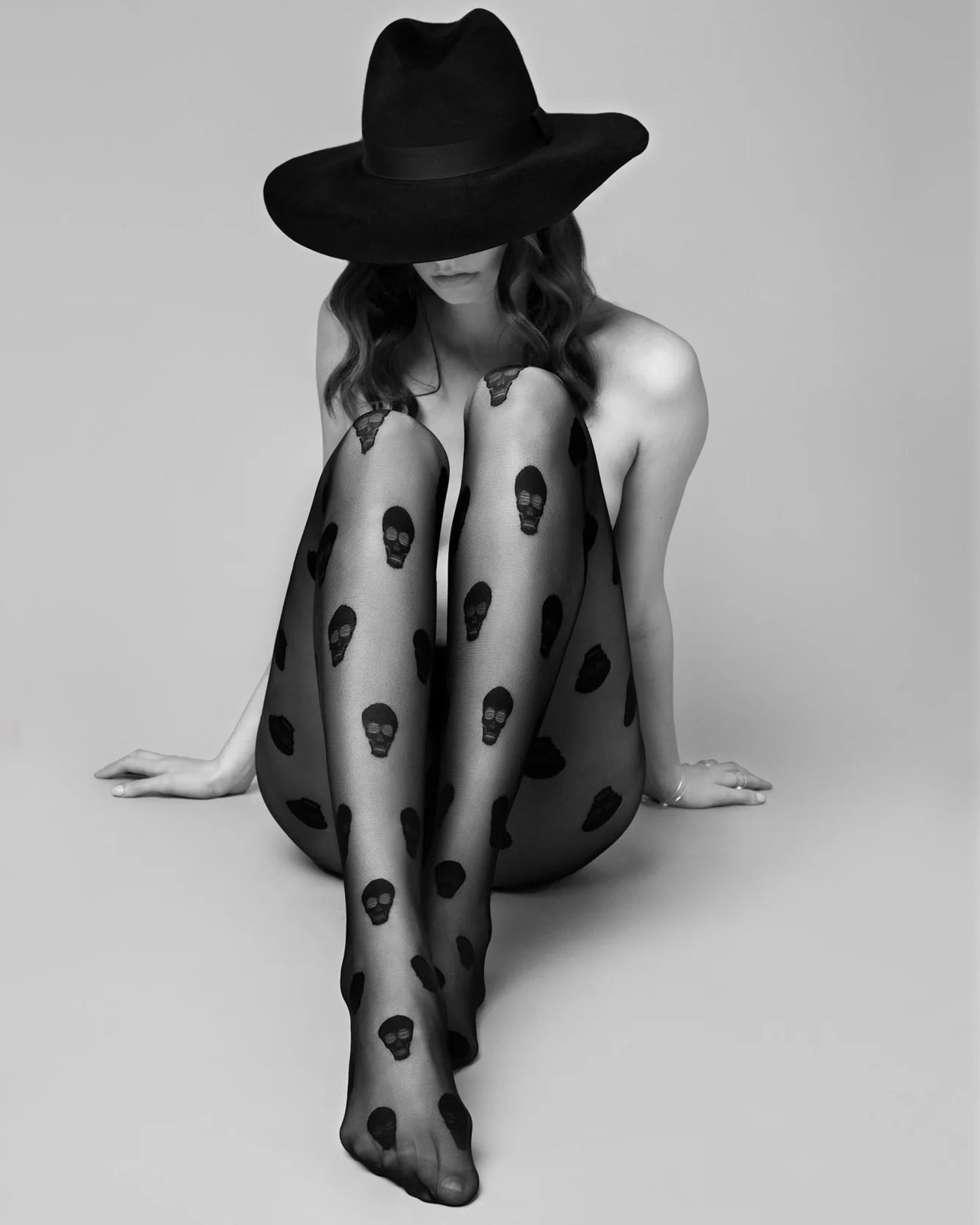 Woman wearing a black fedora hat and sheer black fashion tights with all over skull pattern.