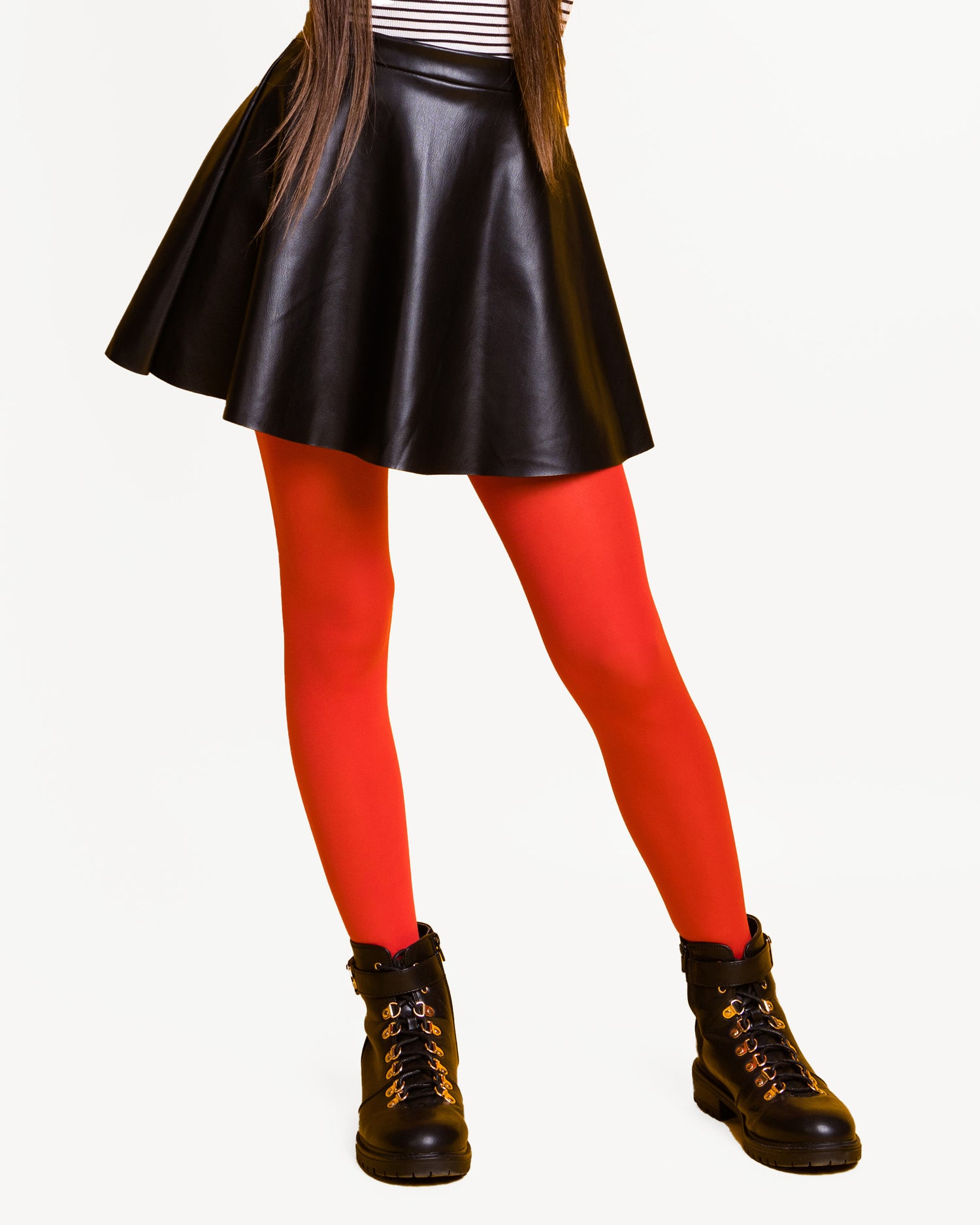 Girl wearing a faux leather skater skirt, white top with black stripes, red tights and black ankle boots.