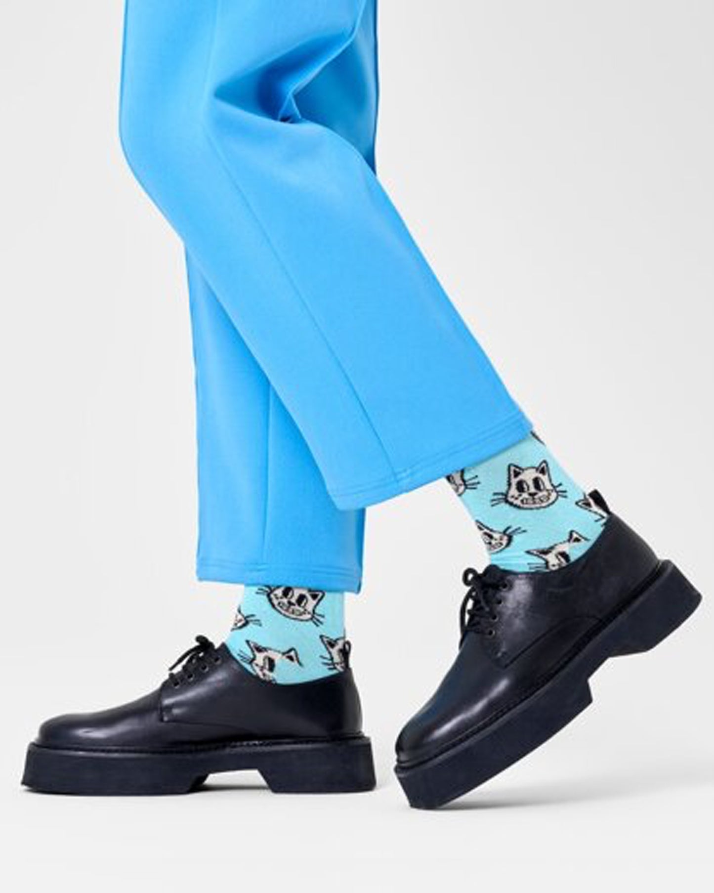 Happy Socks P000721 Cat Sock - Light blue cotton crew length ankle socks with a cartoon cat face pattern in white and black, worn with black brogues and blue cropped pants.