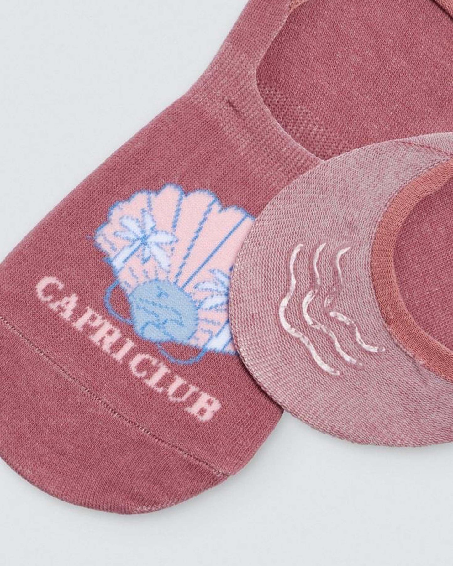 Ysabel Mora Capriclub Shoe Liners - Dirty pink no show shoe liner socks with a clam shell motif with sunset and palm trees in pale pink and light blue, "CAPRICLUB" written underneath and three strips of silicone on the heel.