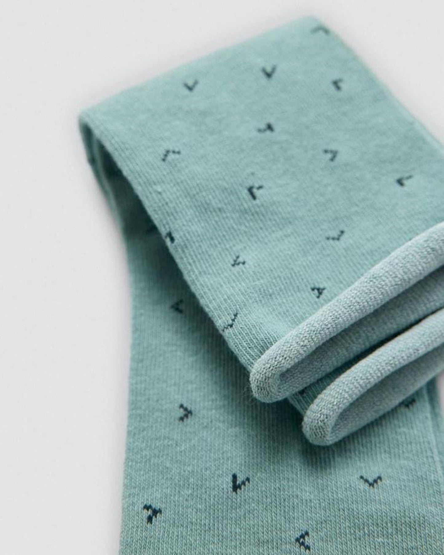 Folded light mint green socks with small black patterns on a white background