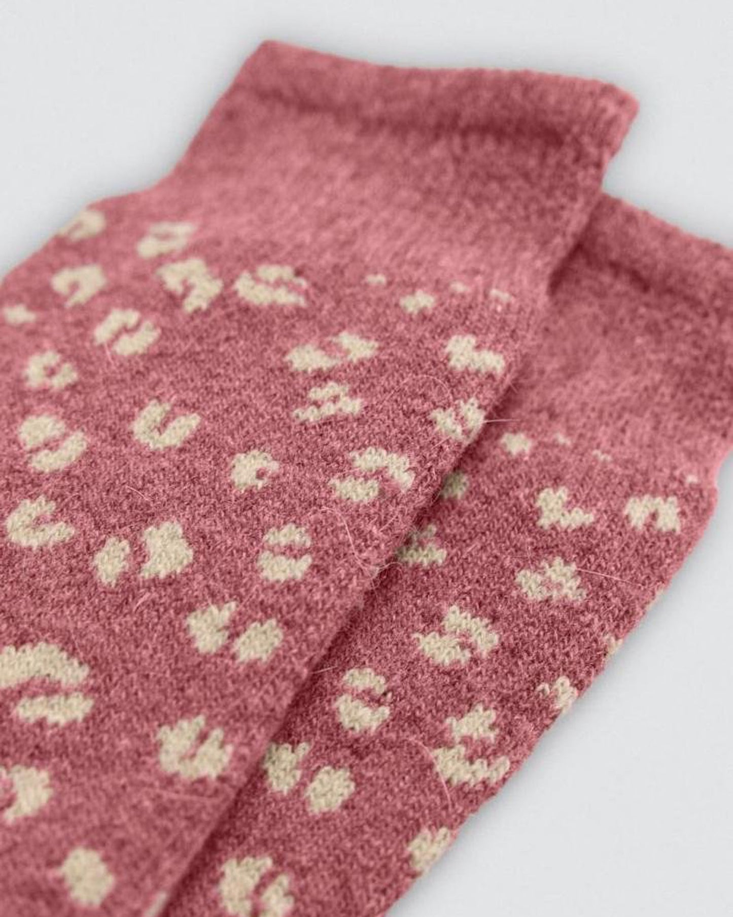 Pink socks with beige patterns on a light gray background, cuff detail.