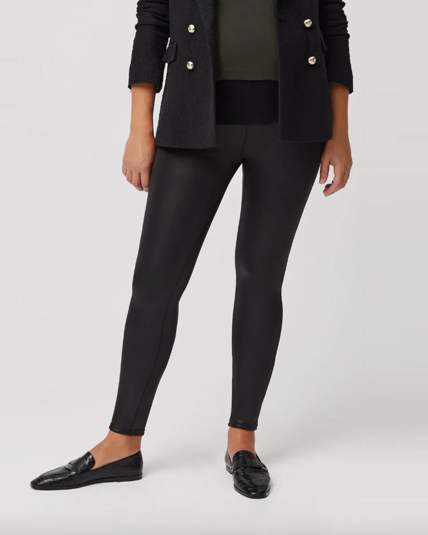 Pregnant woman wearing a black blazer, black leather look maternity leggings and black loafers on a white background