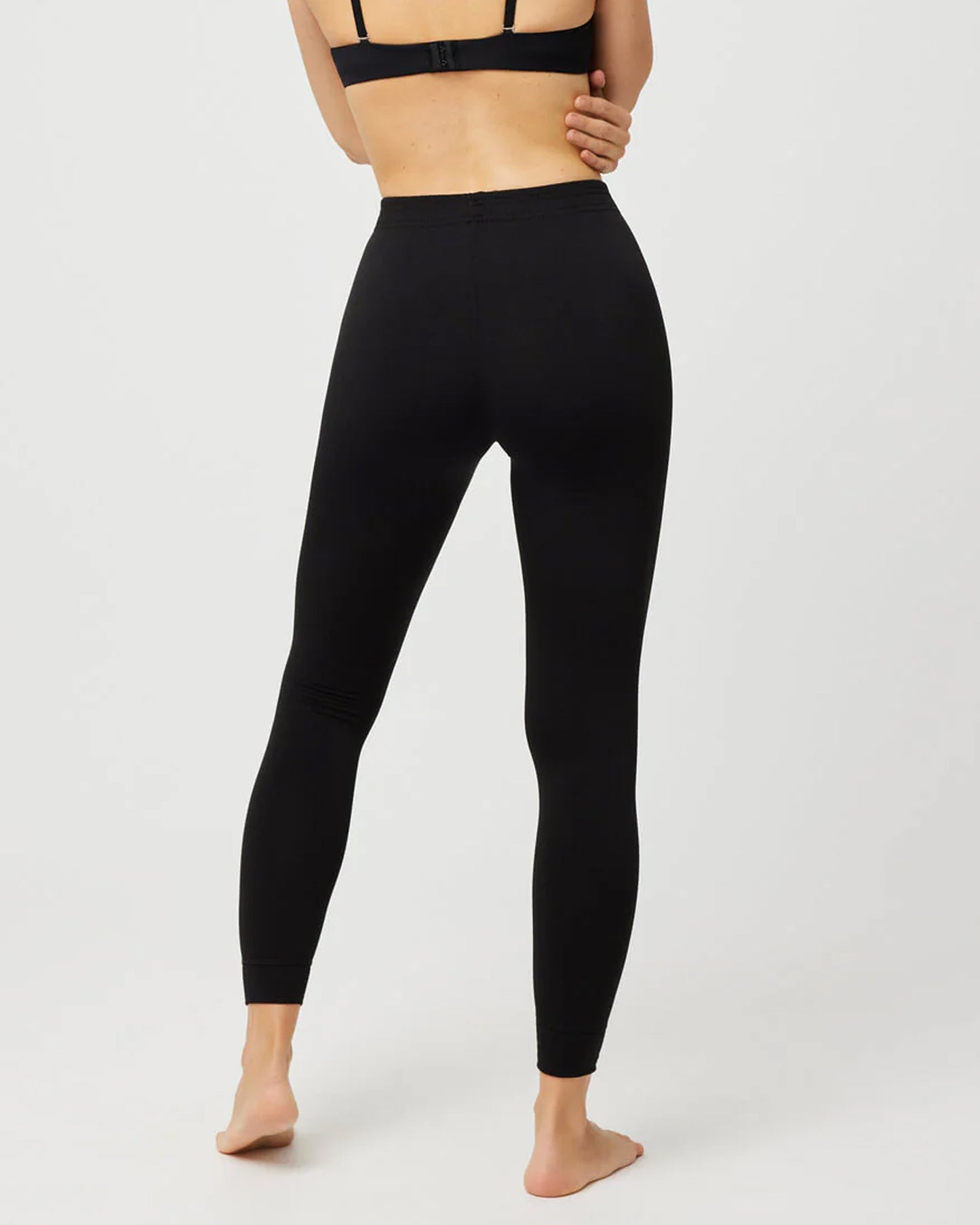 Person wearing black leggings on a white background, back view.