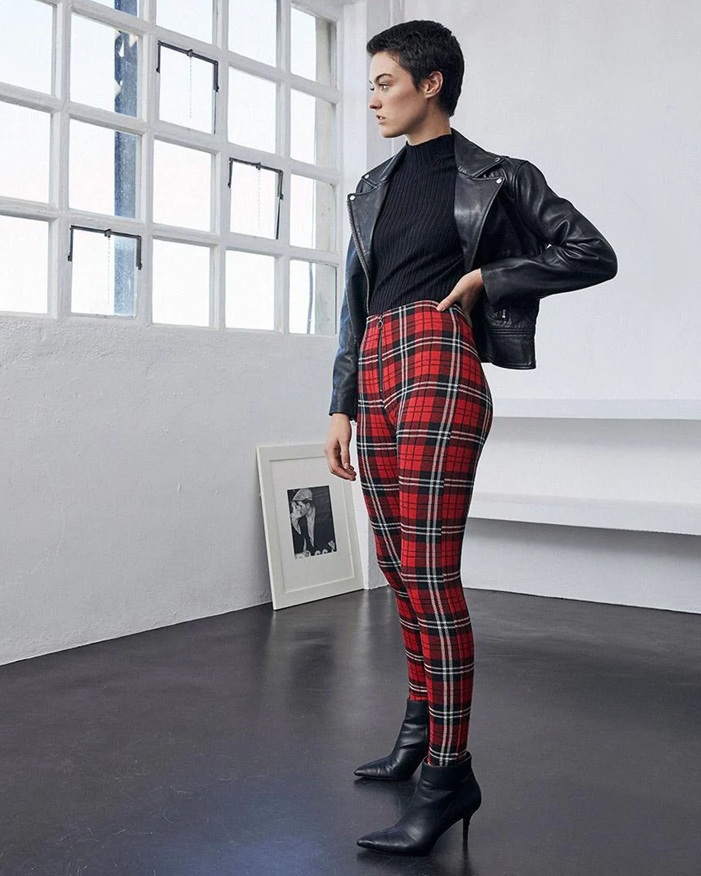 Person wearing a black leather jacket, black top, and red plaid pants in a modern room.