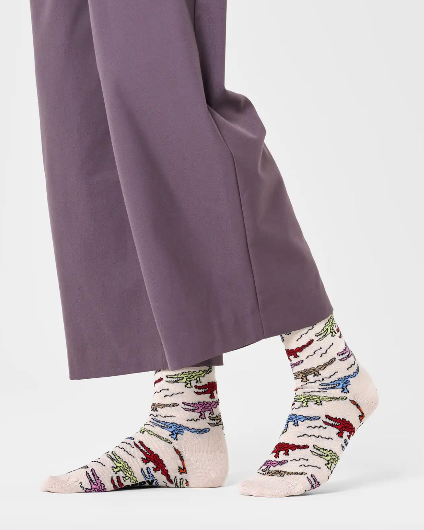 Happy Socks P000713 Crocodile Sock - Cream cotton crew length ankle socks with a multicoloured pattern of crocodiles or alligators. Worn with purple cropped pants.