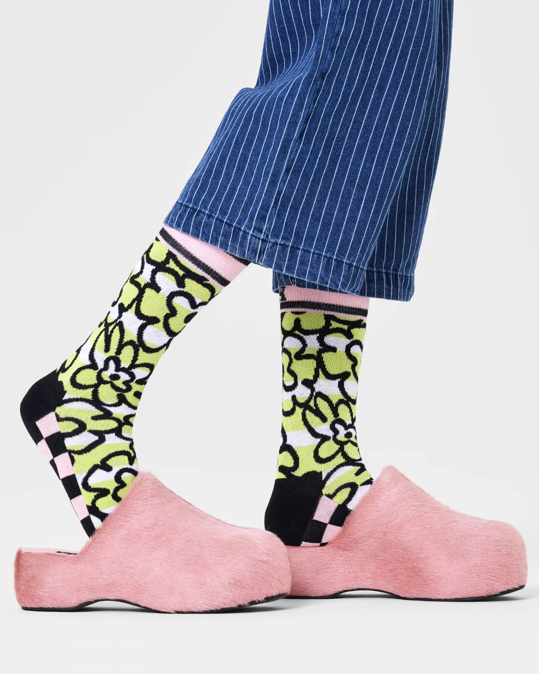 Lime green and white horizontal stripe cotton crew length ankle socks with black outlined flower pattern, black and pink checkerboard pattern sole, pink cuff with black stripe edge and black toe and heel. Worn with fur clogs and denim pinstripe cropped pants.