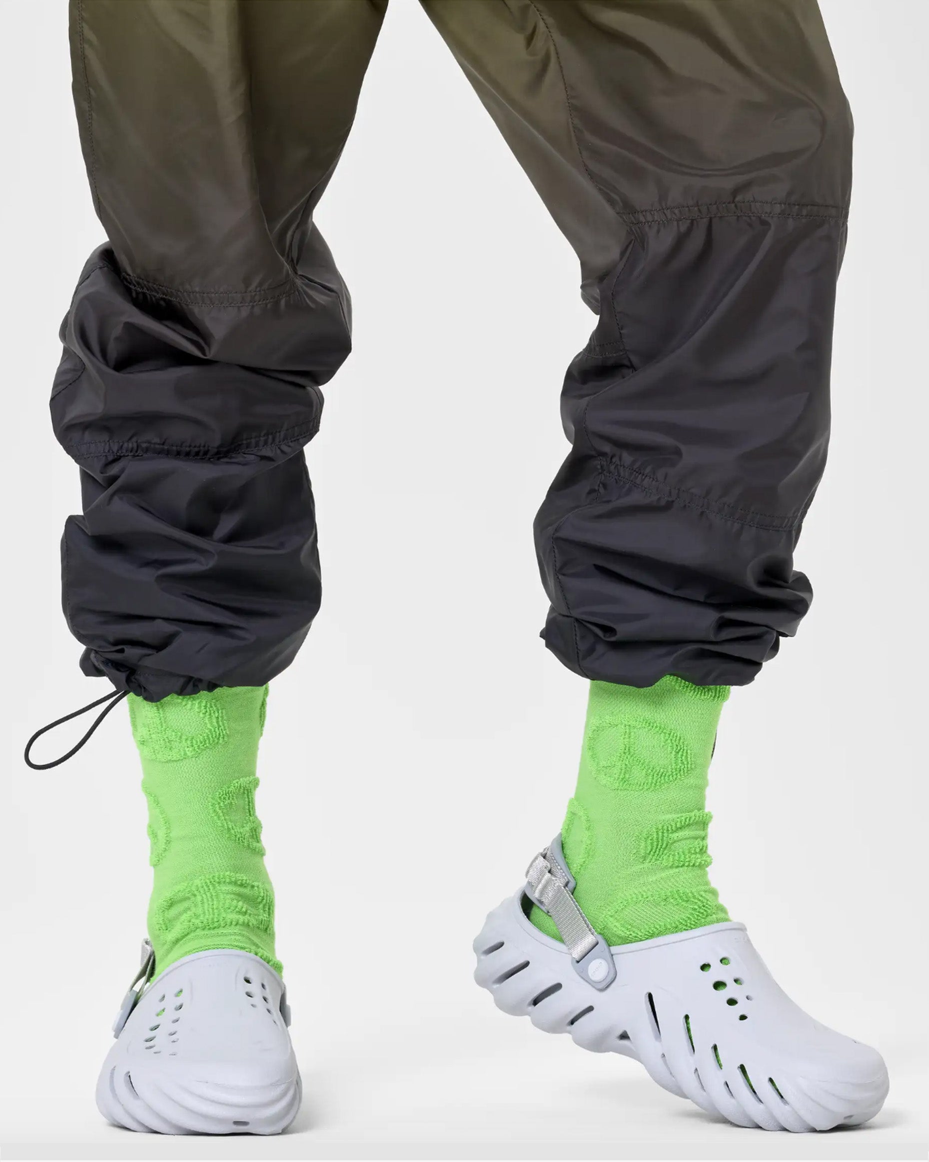 Bright green crew length socks with a textured peace sign pattern. Worn with light grey crocs and gradient elasticated cuff tracksuit pants.