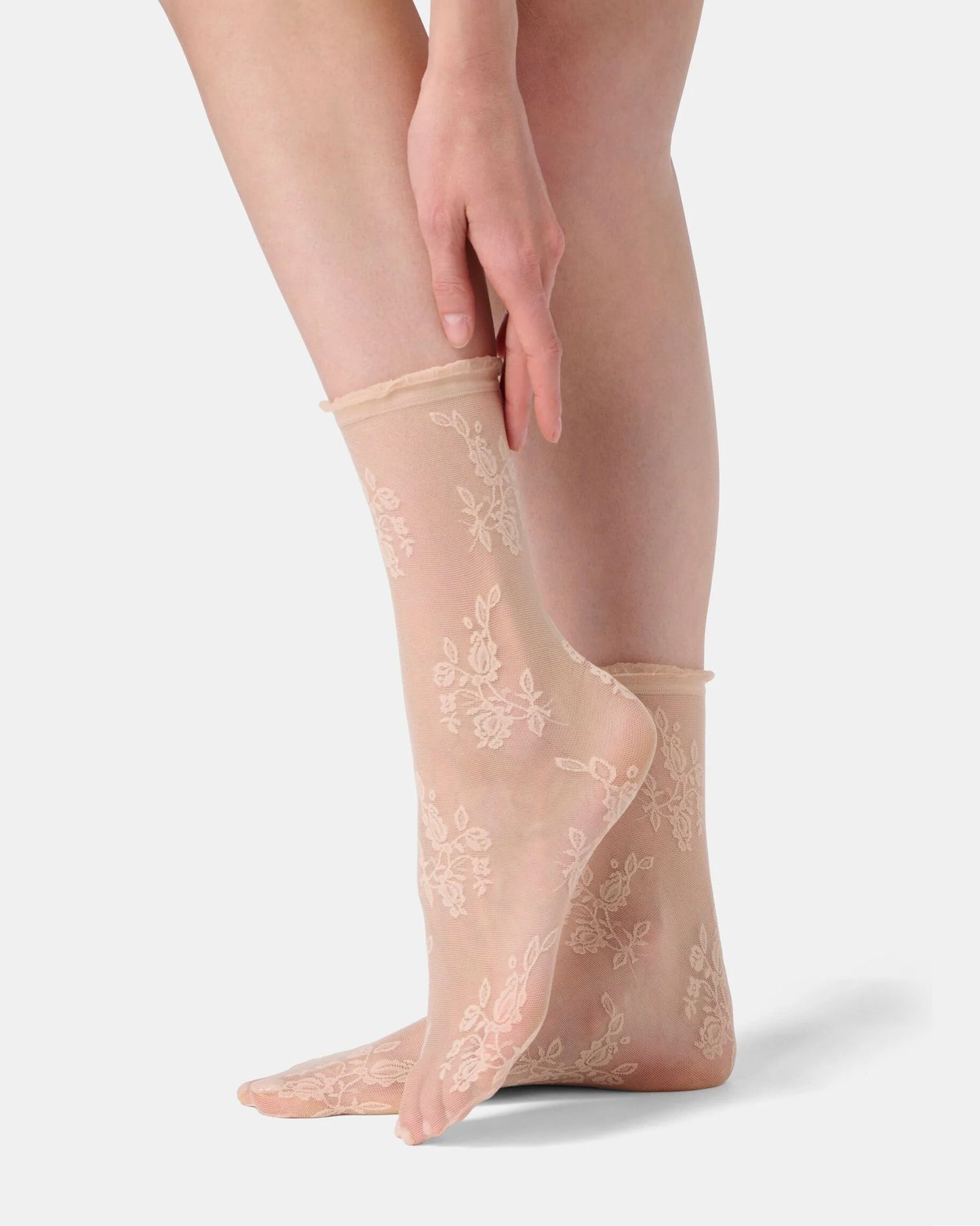 Sheer beige socks with floral lace design worn by a person on a light gray background