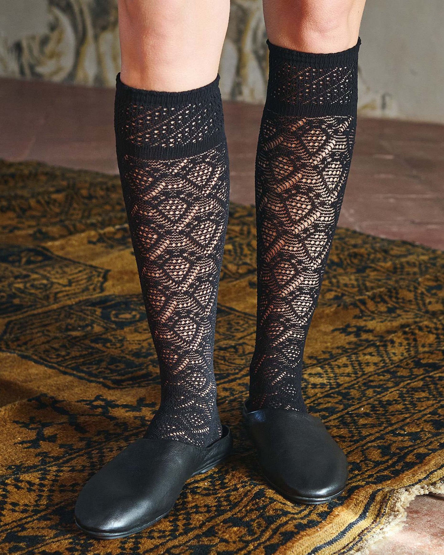 Black coloured crochet lace net style fashion knee-high socks, worn with black leather mules.
