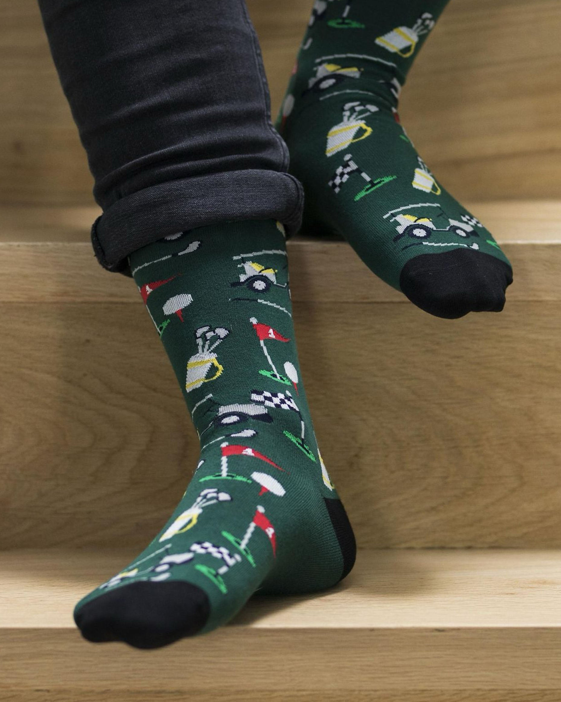 Bonnie Doon Golf Sock - Men's dark green cotton ankle socks with a golf themed pattern of clubs, flags, buggies and balls. Worn with roll up black jeans.