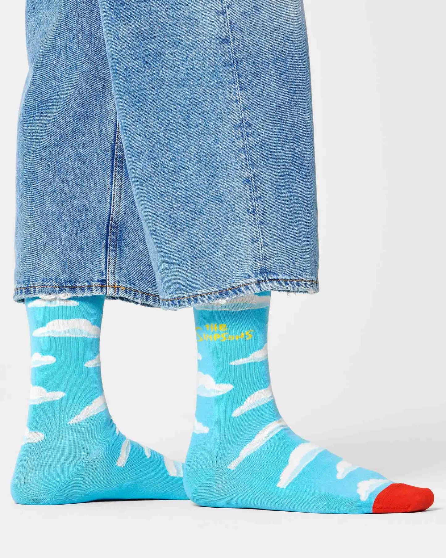 Happy Socks Clouds Socks - The Simpson's themed cotton crew length ankle socks with the opening title scene of clouds and The Simpson's logo in yellow and red toe, worn with cropped denim jeans.
