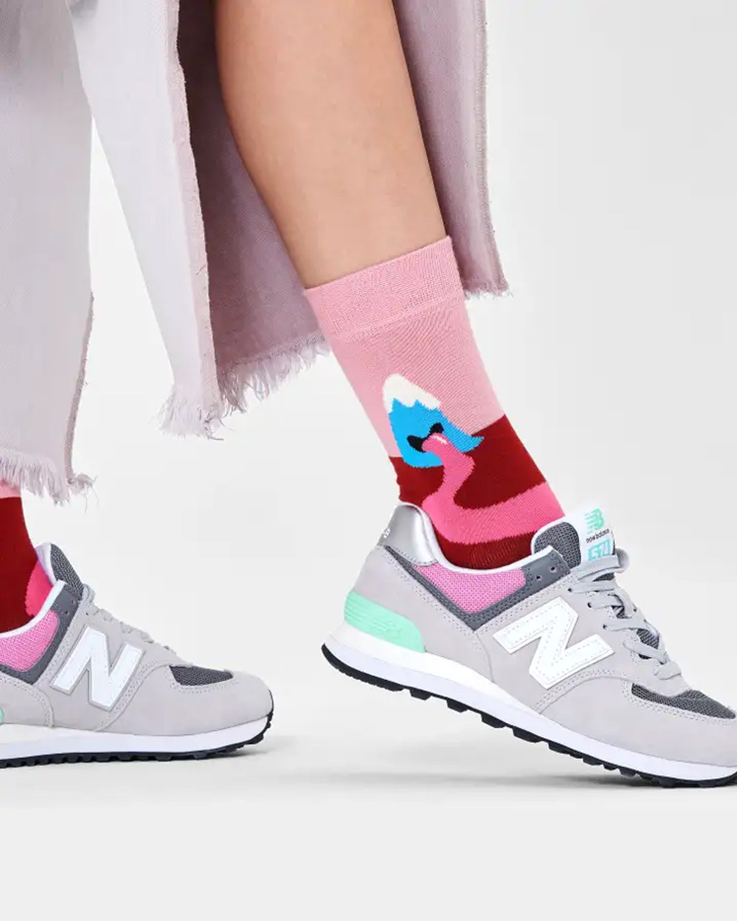 Happy Socks Mountain High Sock - Cotton crew length ankle sock with a personified volcano with pink lava flowing out of its mouth onto a maroon coloured ground against a pale pink sky worn with trainers and cut off denim jeans.