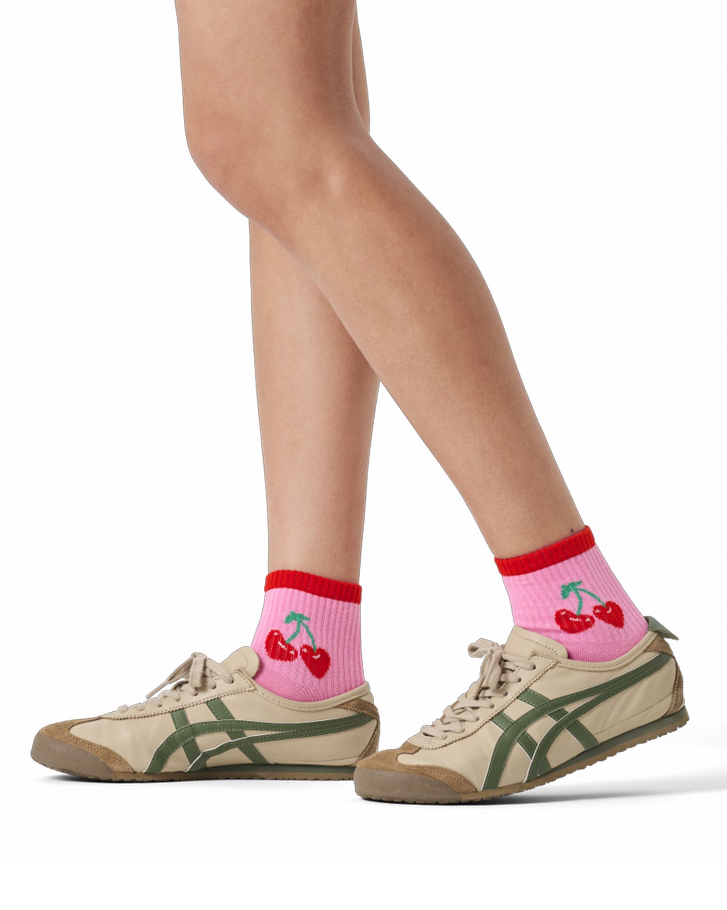 Person wearing pink socks with cherry design and green sneakers on a white background