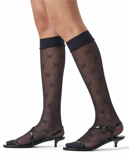 Black knee-high sheer socks with a pattern and black shoes on a white background