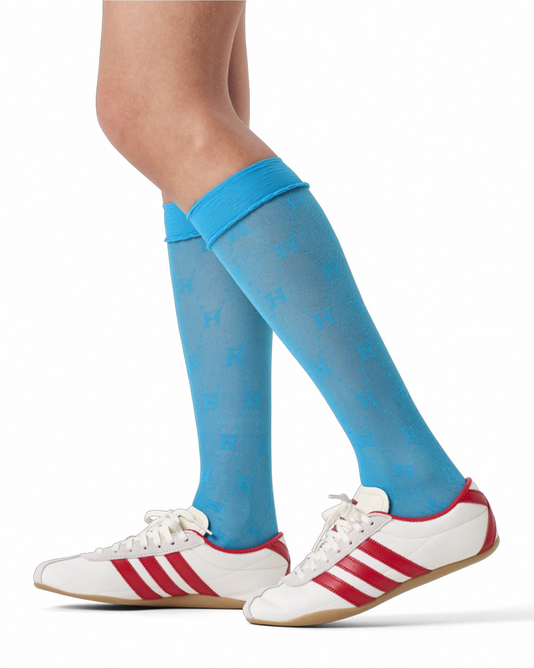 Blue knee-high socks with a pattern worn with white sneakers featuring red stripes on a white background.