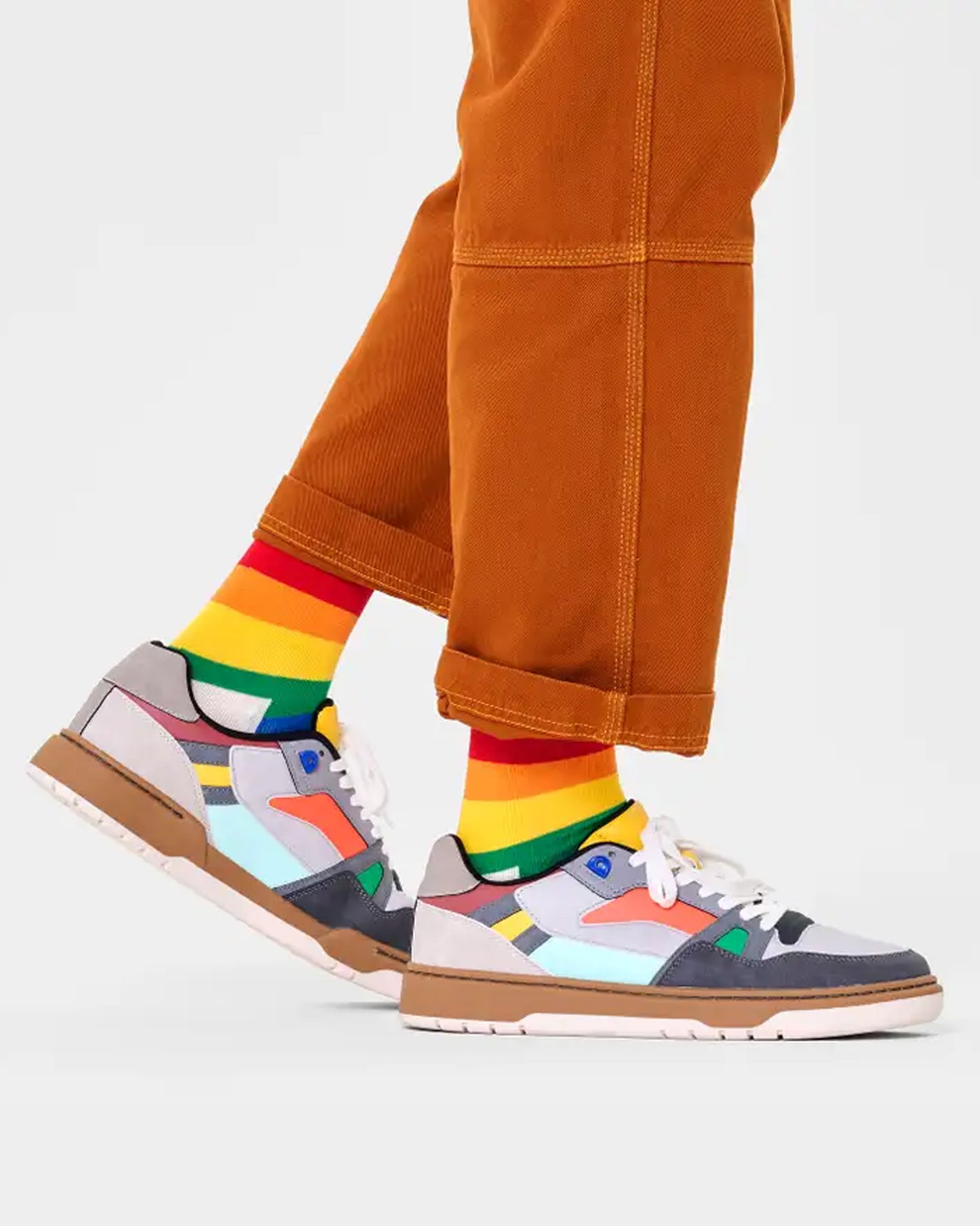 Happy Socks PRS01-0200 Pride Sock - Cream organic cotton crew length ankle socks with a horizontal LGBTQ+ rainbow stripe pattern. Worn with sneakers and orange trousers.
