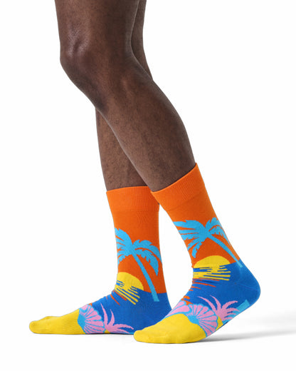 Colorful socks with palm tree design worn by a person on a white background