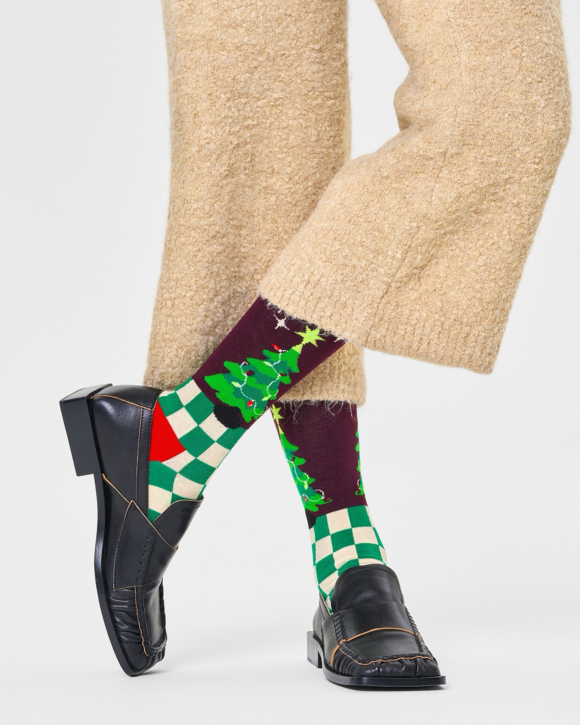 Happy Socks P000262 Christmas Tree Socks - Checkered green and cream socks with a Xmas tree motif on the top (inside and outside) with a burgundy background, red heel. Worn by a woman wearing beige knitted cropped pants and black loafers.