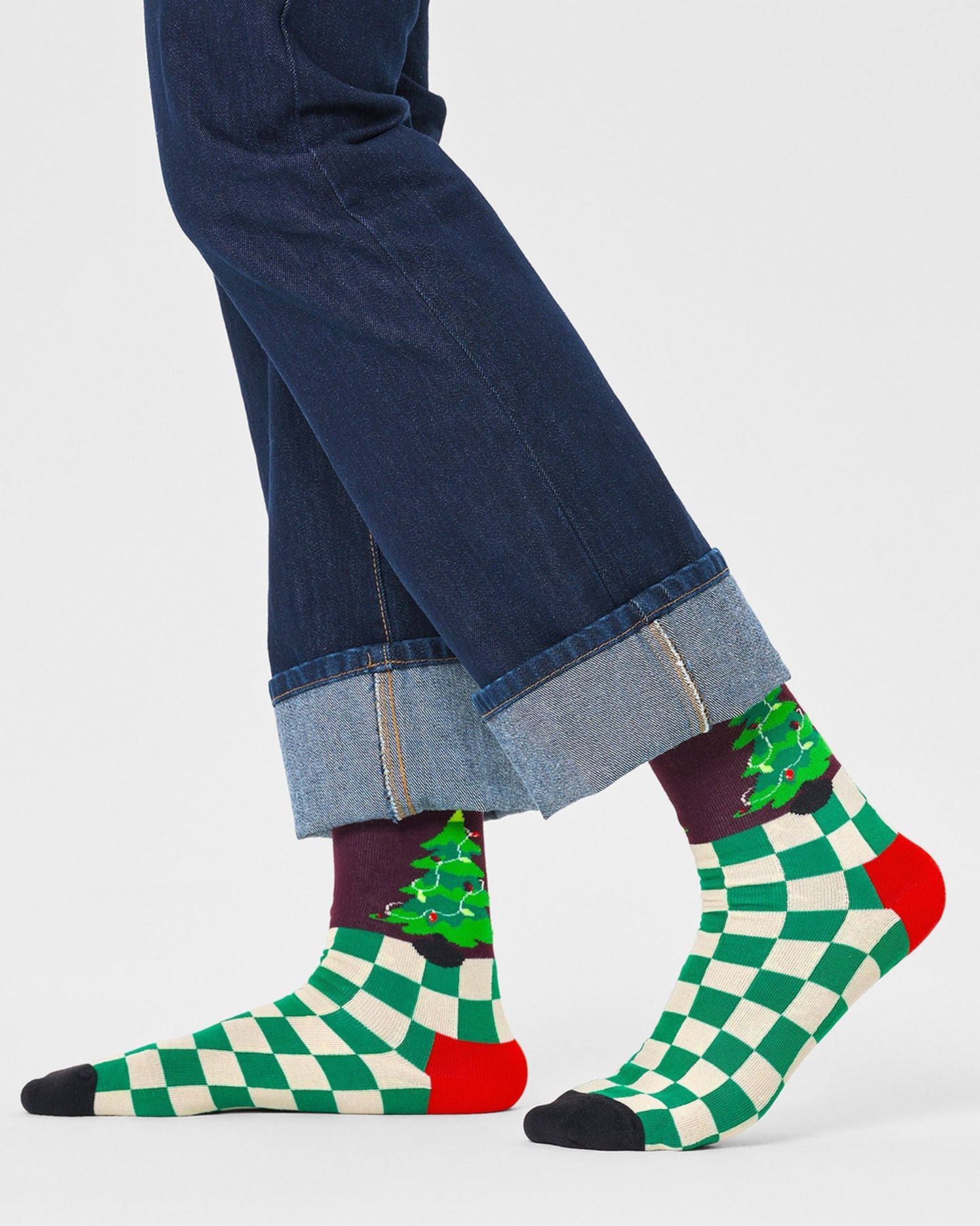Happy Socks P000262 Christmas Tree Socks - Checkered green and cream socks with a Xmas tree motif on the top (inside and outside) with a burgundy background, red heel and black toe. Worn by a man wearing turned up denim jeans.