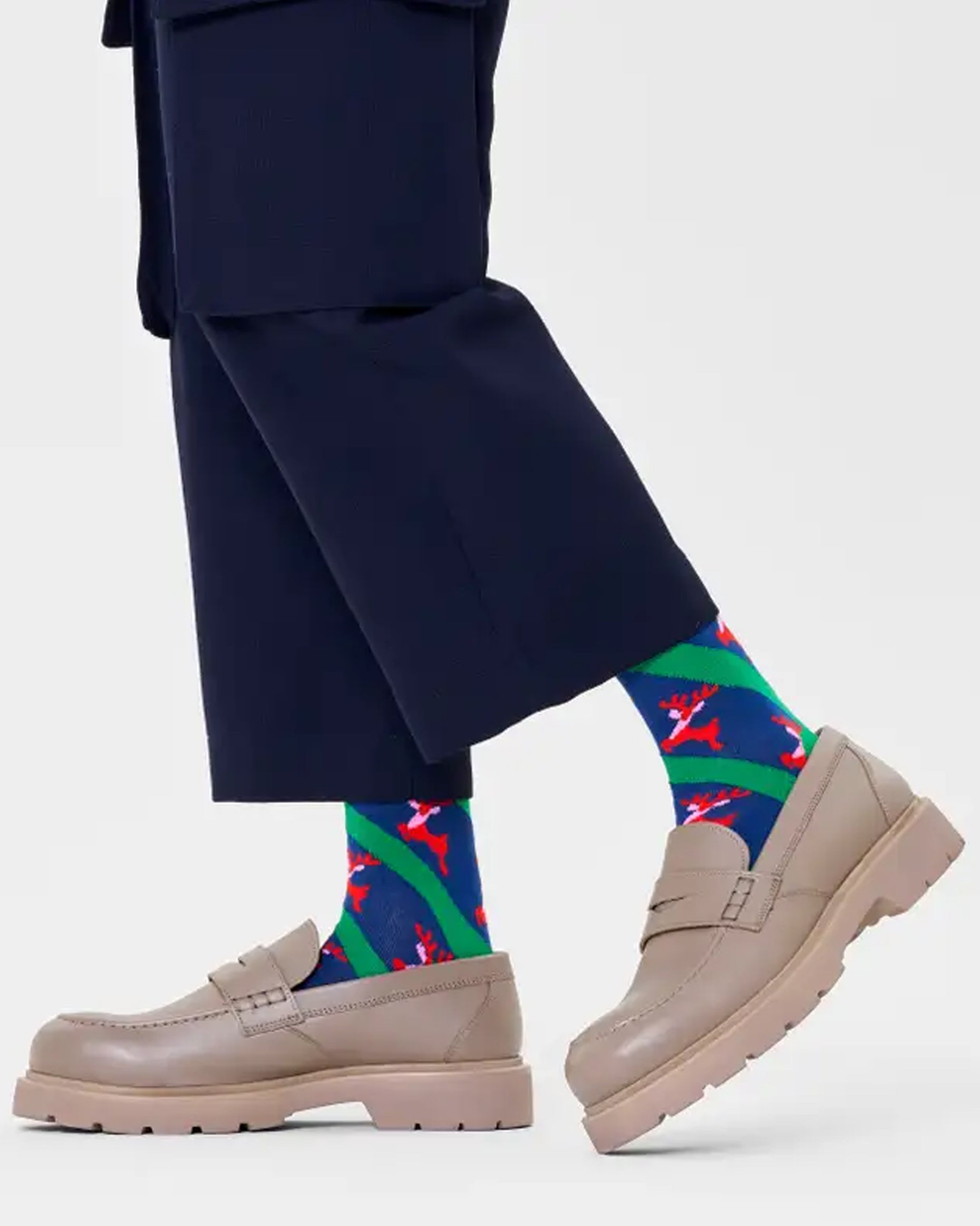 Happy Socks P000264 Reindeer Socks - Navy blue cotton crew length socks with green diagonal stripes and red reindeers pattern, green toe, heel and cuff. Worn with navy cropped pants and chunky beige loafers.