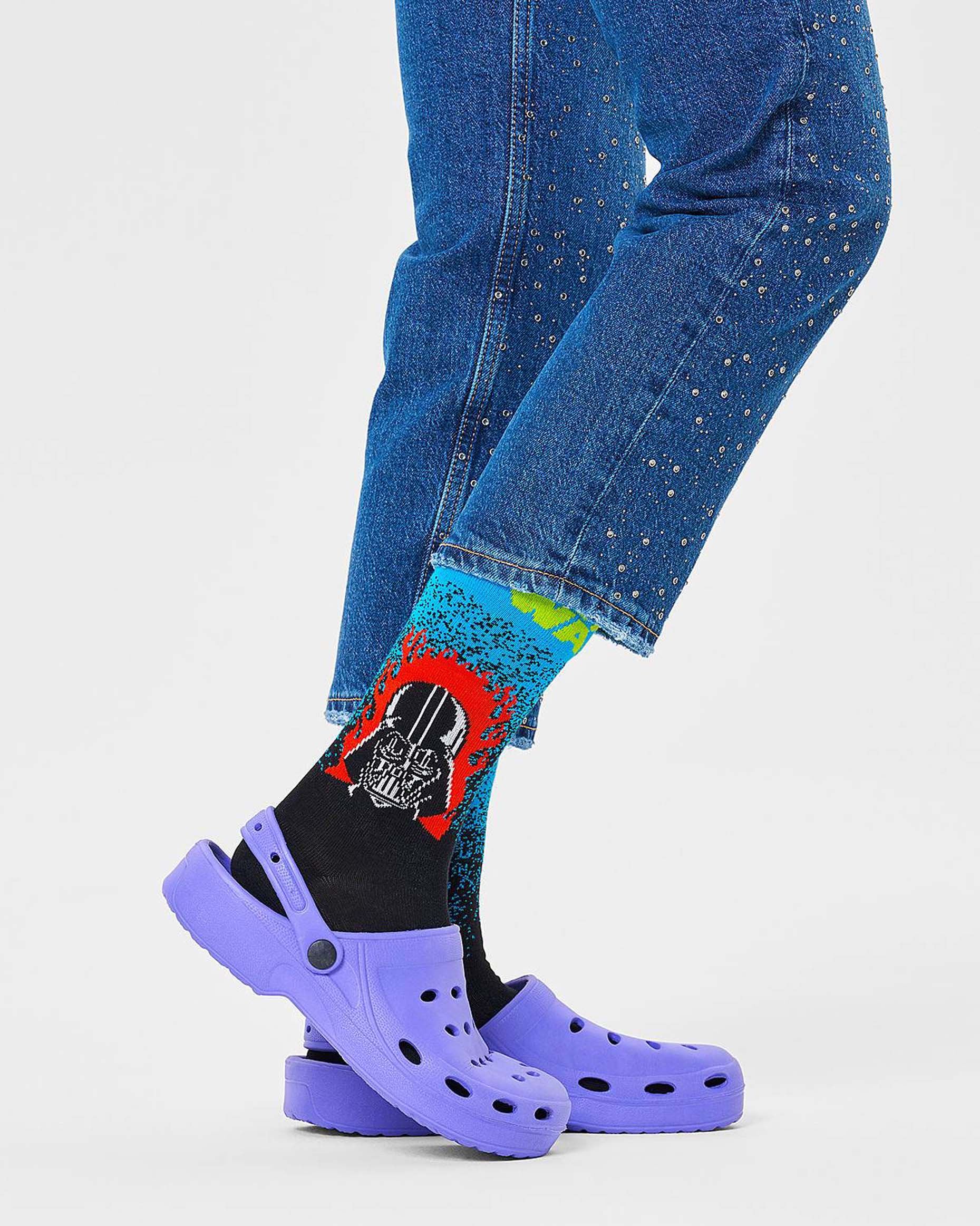 Happy Socks Darth Vader Sock - Women's cotton crew socks with an ombre/gradient effect going from blue on the top to black with a Darth Vader motif with flames in red, black and white and Star Wars logo in bright neon green worn with purple crocs and studded denim jeans.