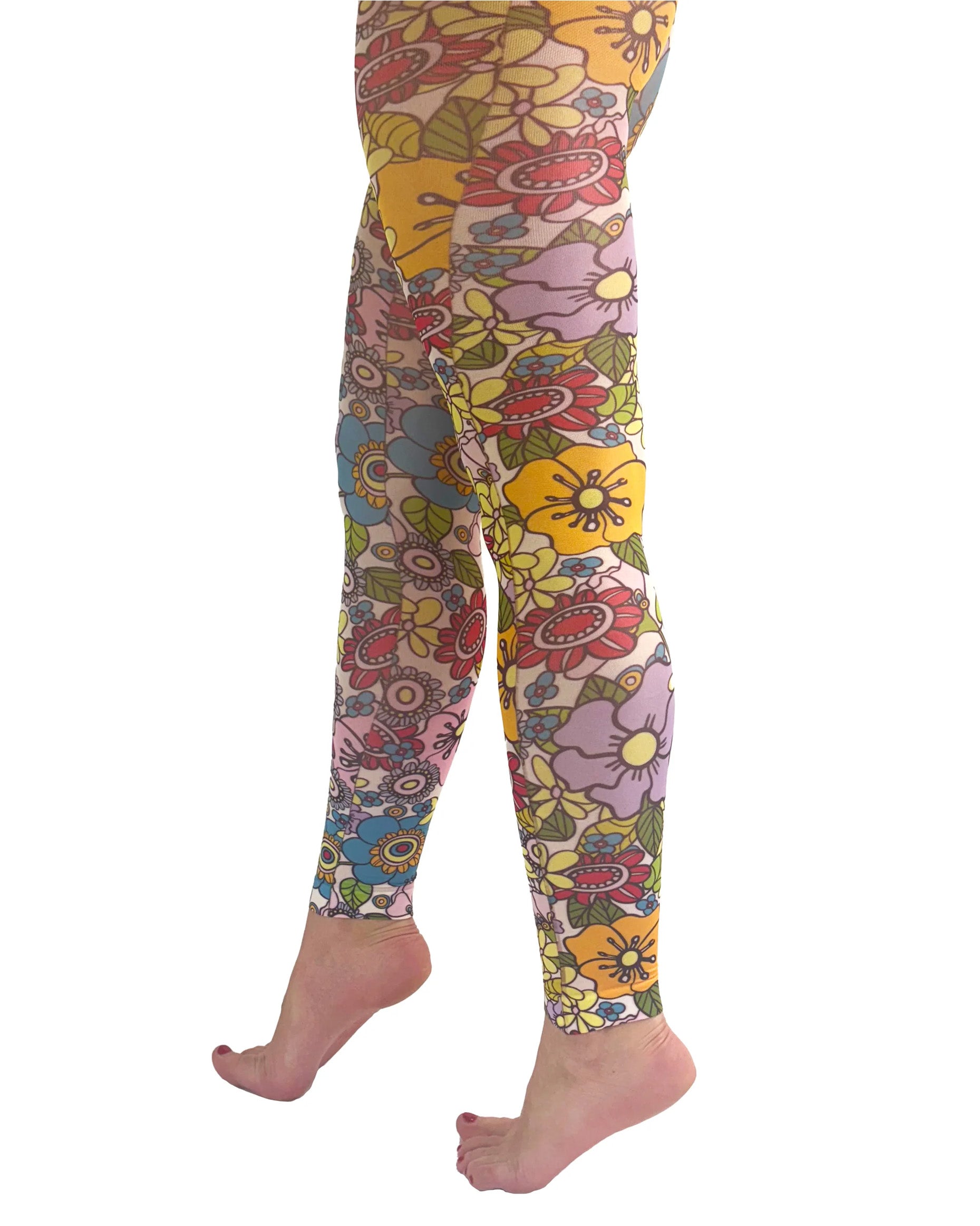 Pamela Mann Flower Power Footless Tights - Pale pink opaque footless tights with a sixties style flower print pattern in bright shades of purple, yellow, blue, red, pink, orange and outlined in black. Side view.