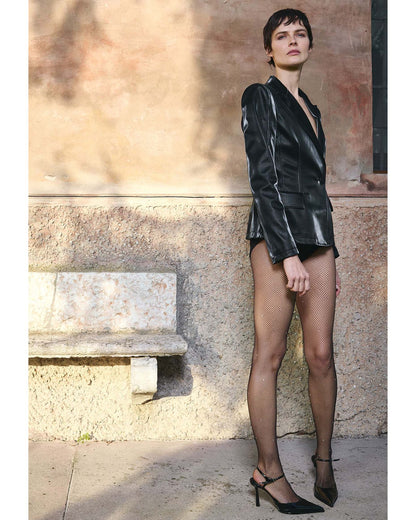 Woman in a black outfit and black crystal fishnets standing against a stone wall.