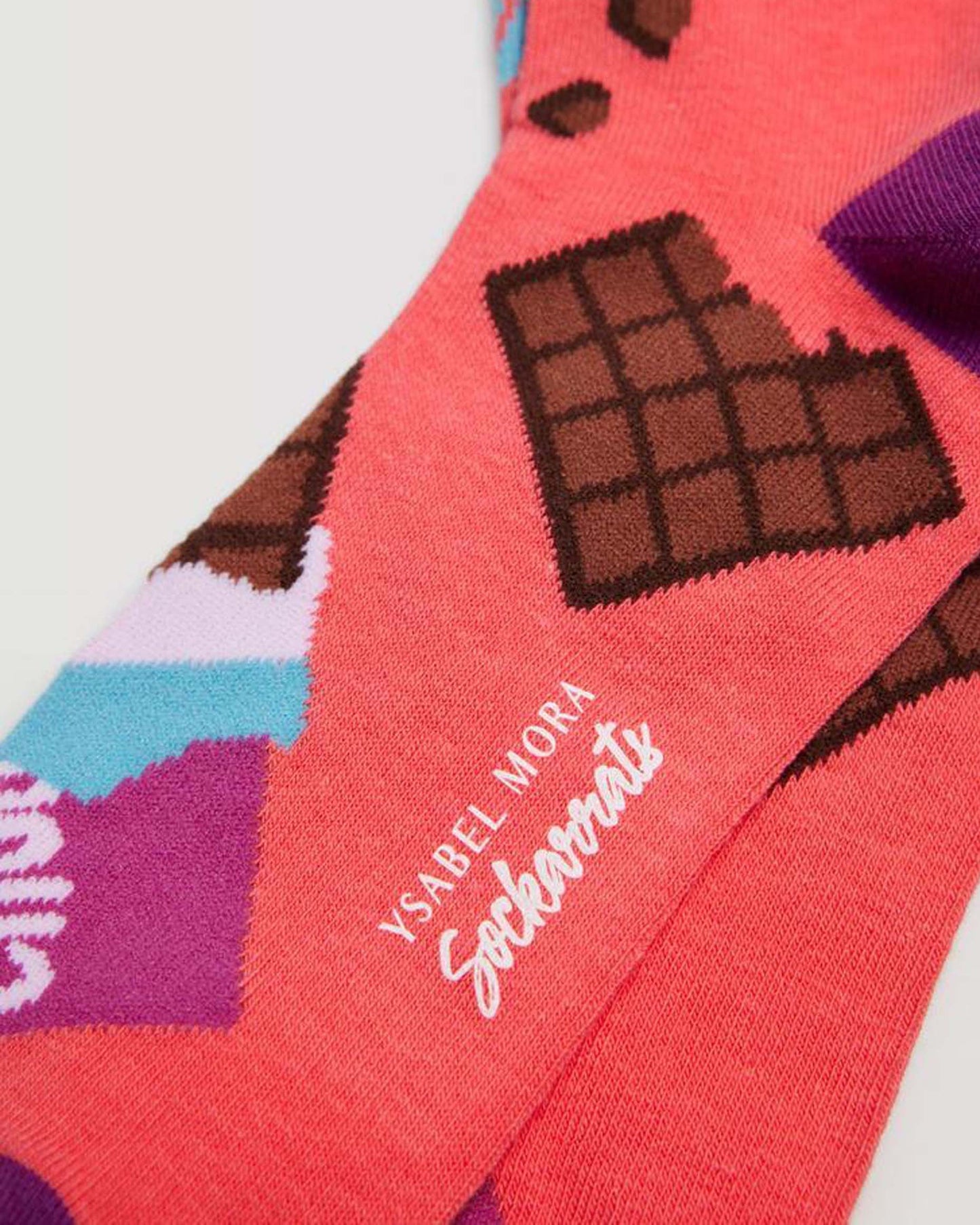 Ysabel Mora Sockarrats Chocolate Bar Socks - Bright coral coloured cotton socks with an all over pattern of chocolate bars pattern in brown, turquoise, purple and black, purple heel.
