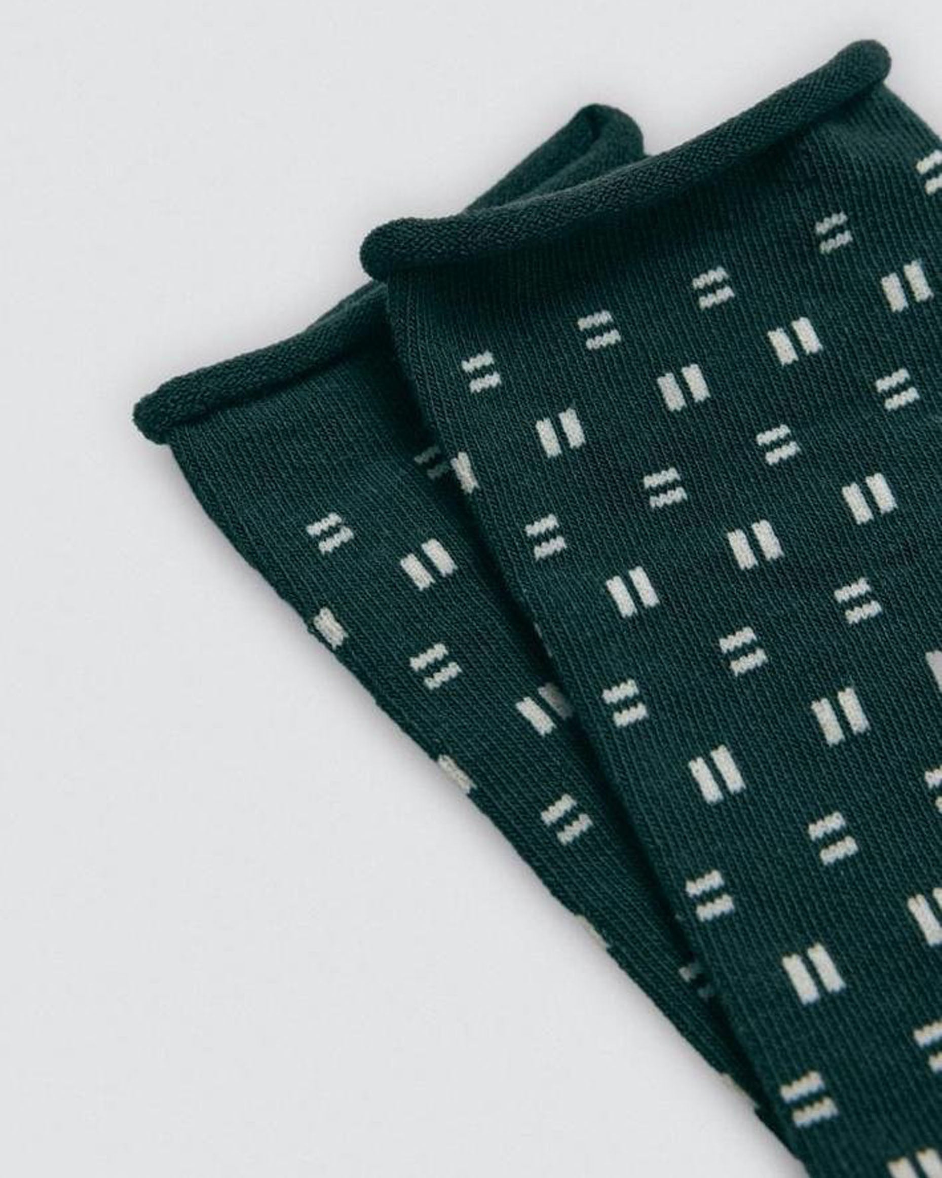 Dark green socks with white geometric pattern on a light gray background