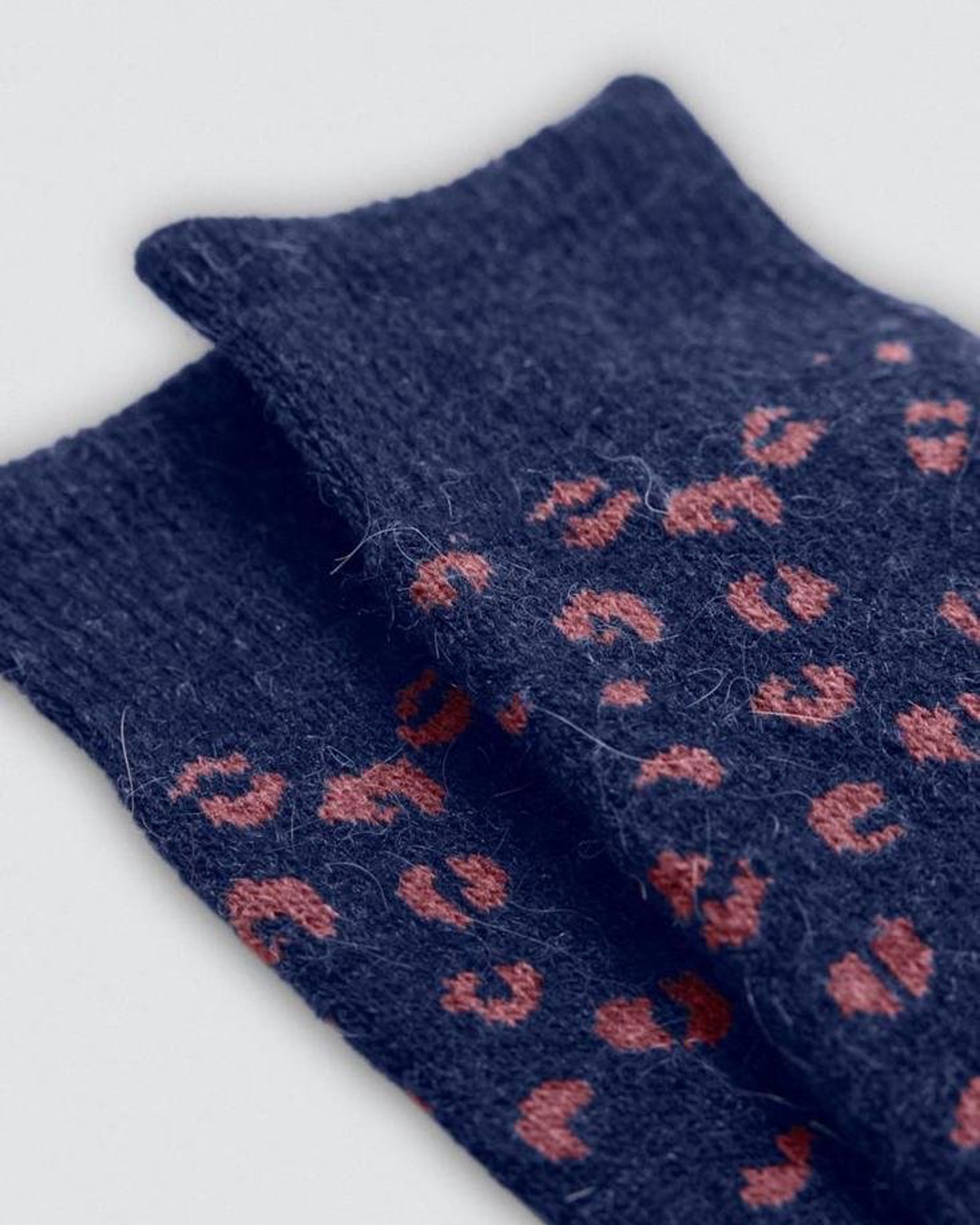 Pair of blue socks with red pattern on a light gray background, cuff detail.