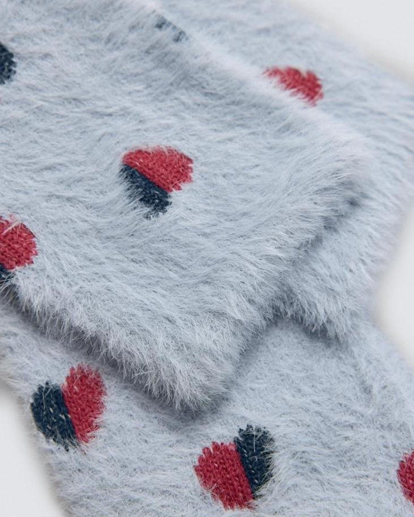 Close-up of a fluffy blue ankle socks with red and black heart patterns.