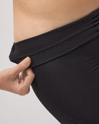 Person folding down the waist band of thermal fleece lined black tights on a plain background
