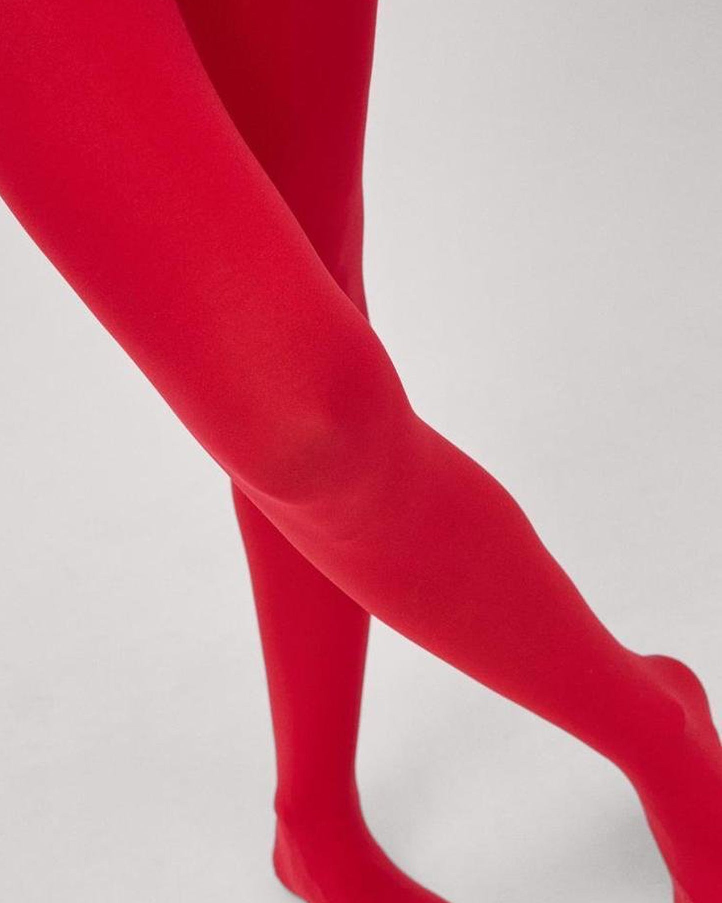 Close up of red opaque tights worn by a model with light grey backdrop
