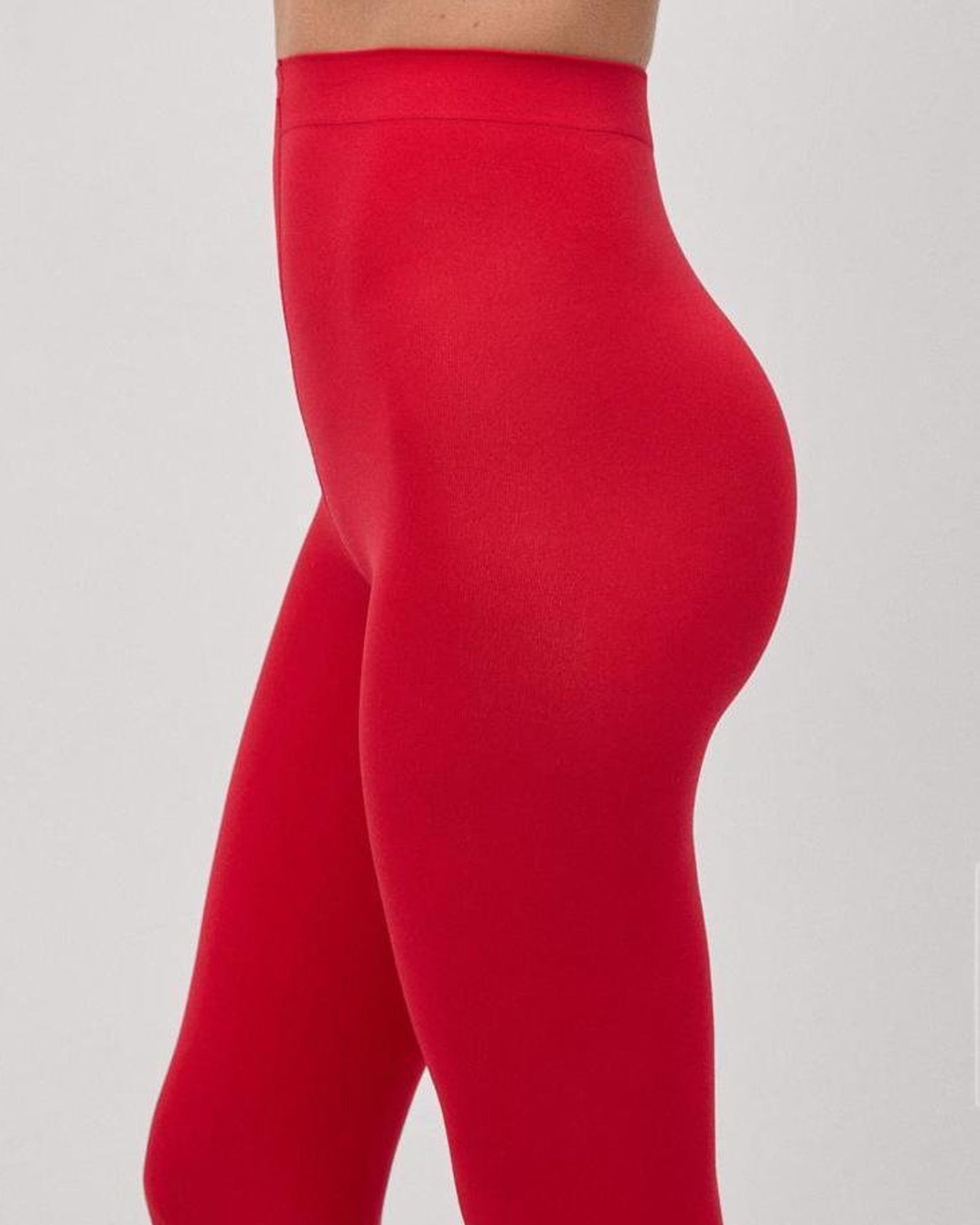 Close up of waist of red opaque tights worn by a model with light grey backdrop