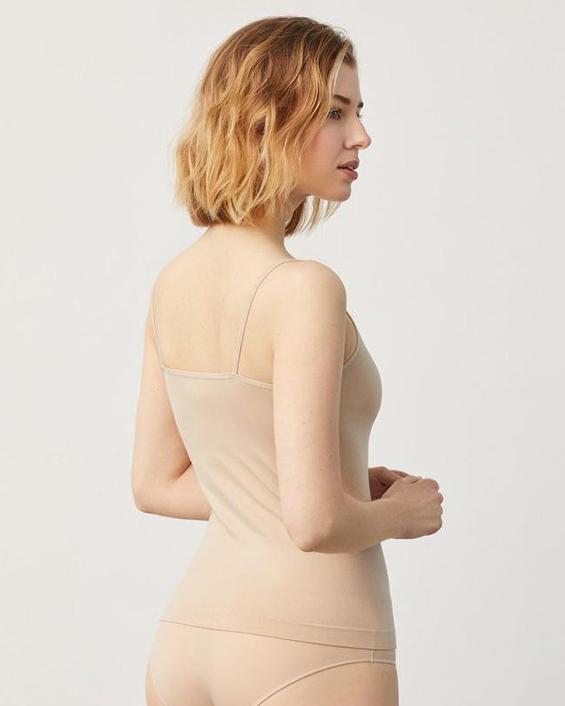 Woman wearing a beige string top and briefs against a plain background. Back view.