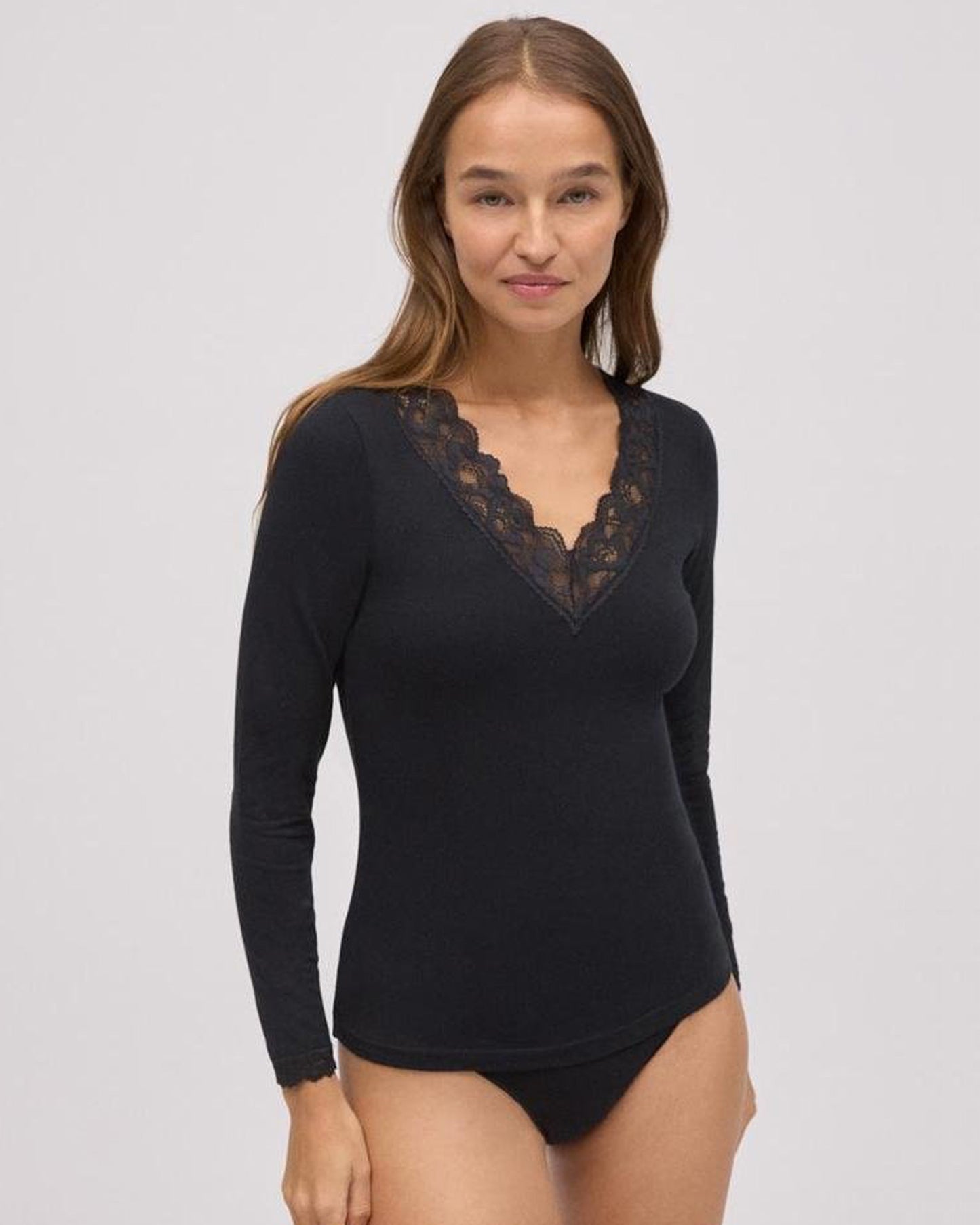 Woman wearing a black long-sleeve top with lace neckline on a gray background
