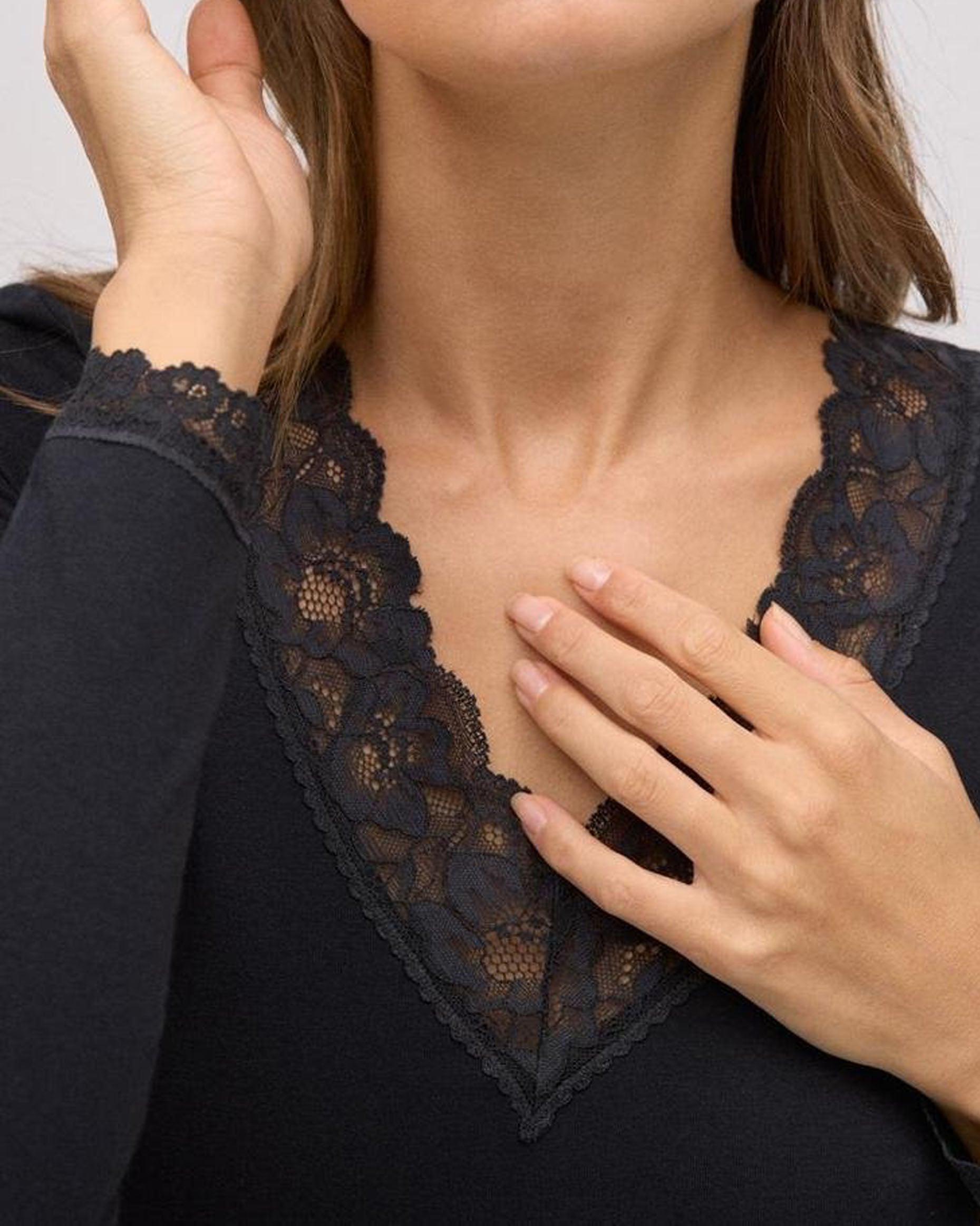 Close-up of a person wearing a black lace top with hands adjusting the neckline.