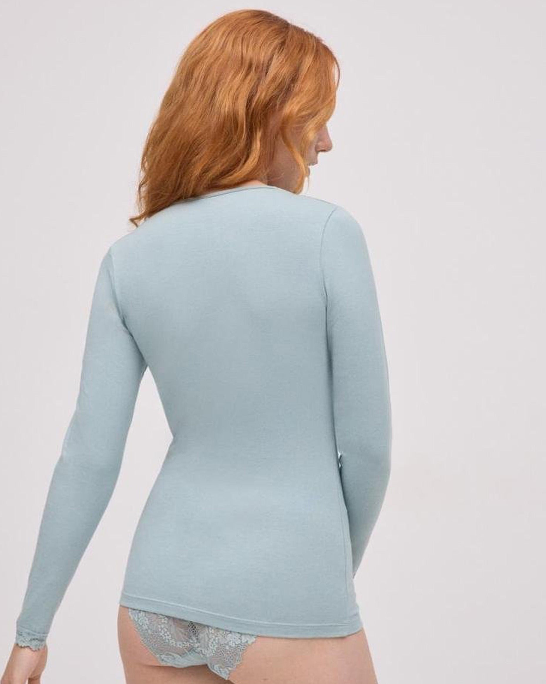 Woman wearing a light blue long-sleeve shirt against a plain, back view.background