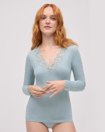 Woman wearing a light mint green bodysuit with lace detailing on a plain background