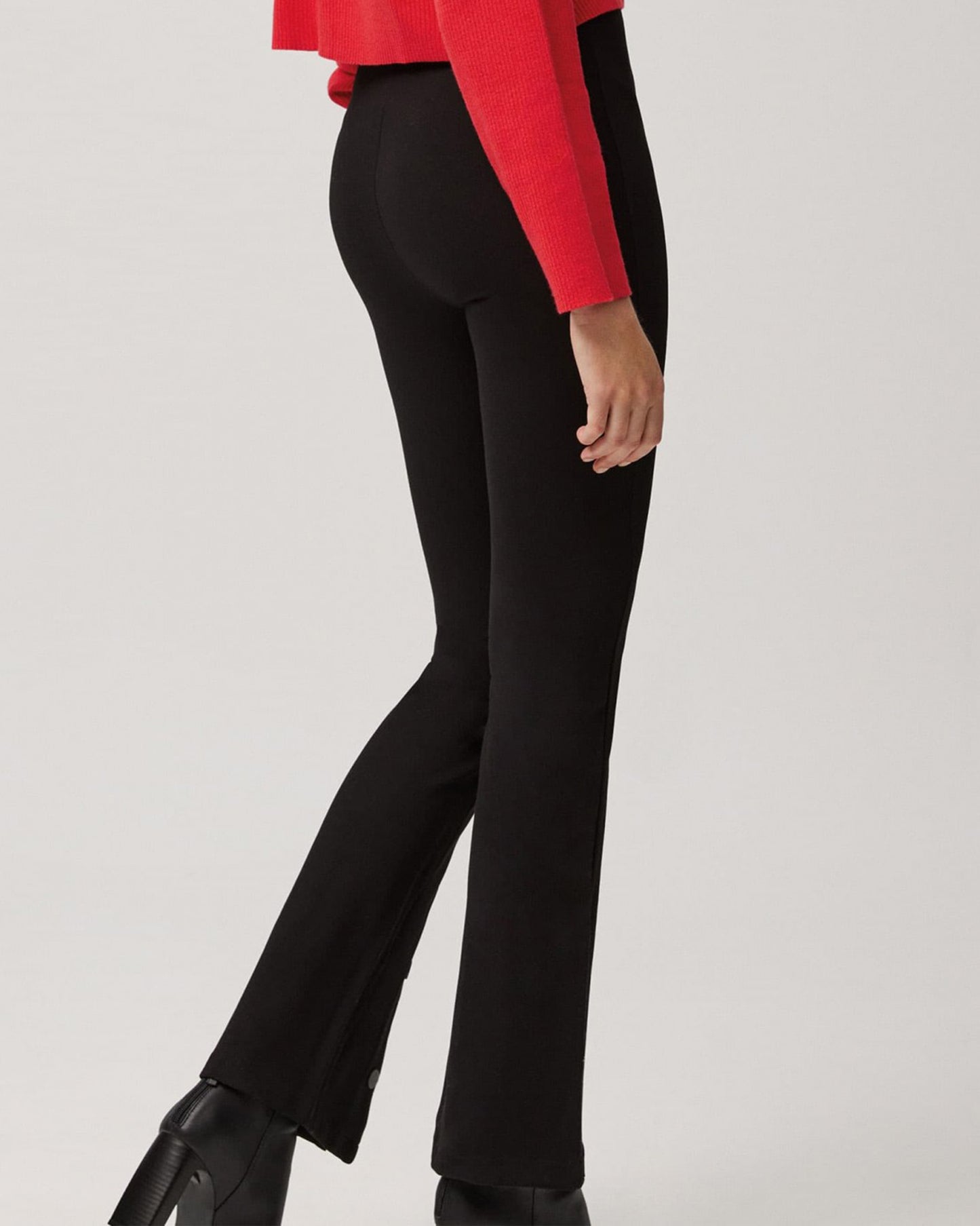 Ysabel Mora 70153 Flared Button Leggings - Black high waisted stretch trouser leggings (treggings) with split buttoned flare bottom. Worn with red sweater and black ankle boots. Back view.