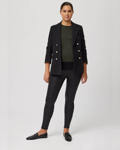 Pregnant woman wearing a black blazer with gold buttons, khaki green top, black waxed look pants and black shoes on a white background