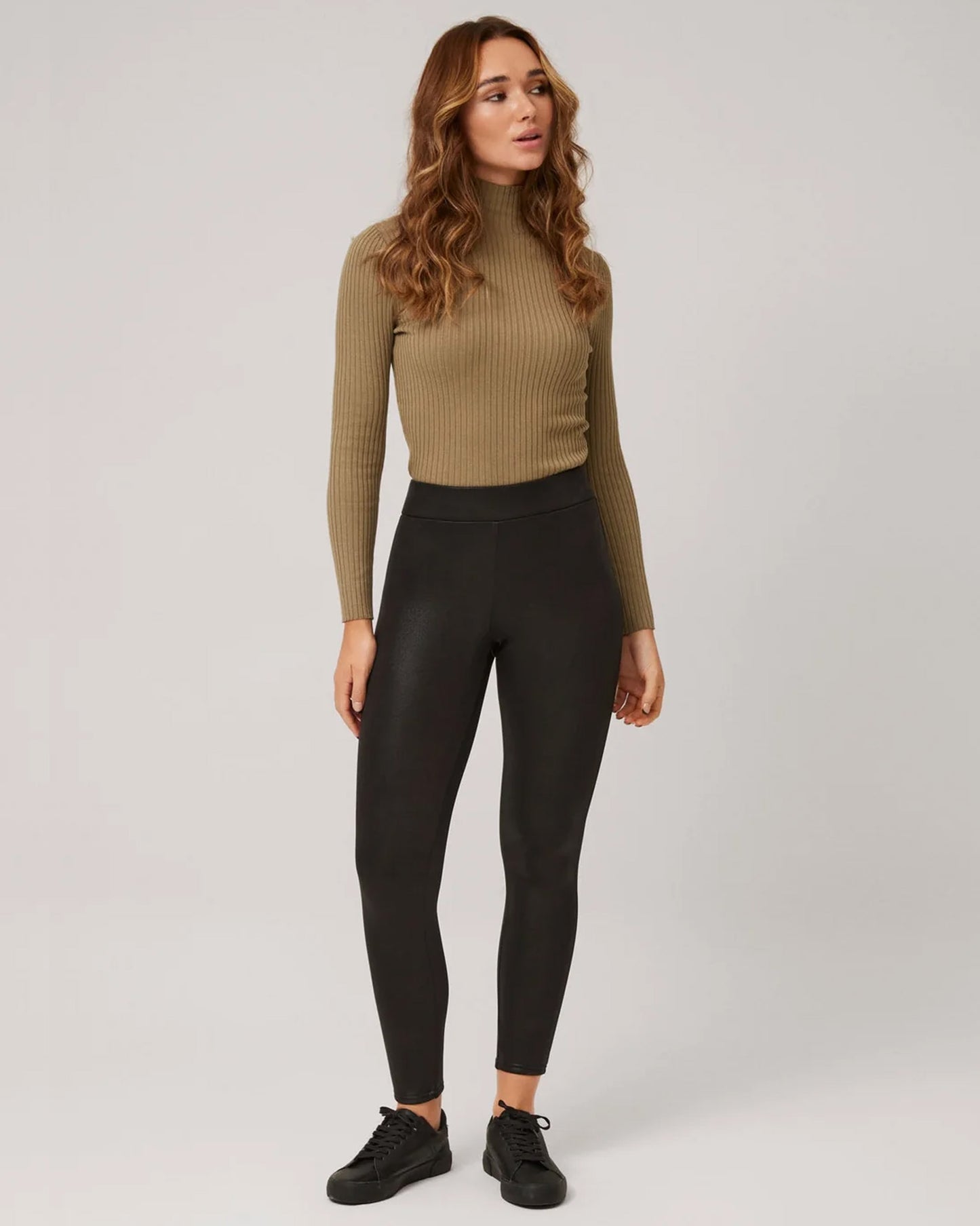 Ysabel Mora 70293 Waxed Thermal Leggings - Woman wearing a beige ribbed turtle neck top, tucked into black high waisted thermal trouser leggings with waxed effect print and black sneakers.