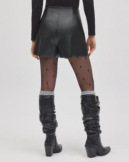 Person wearing a black leather skort, black knee-high boots, and black tights with star patterns on a white background, back view.