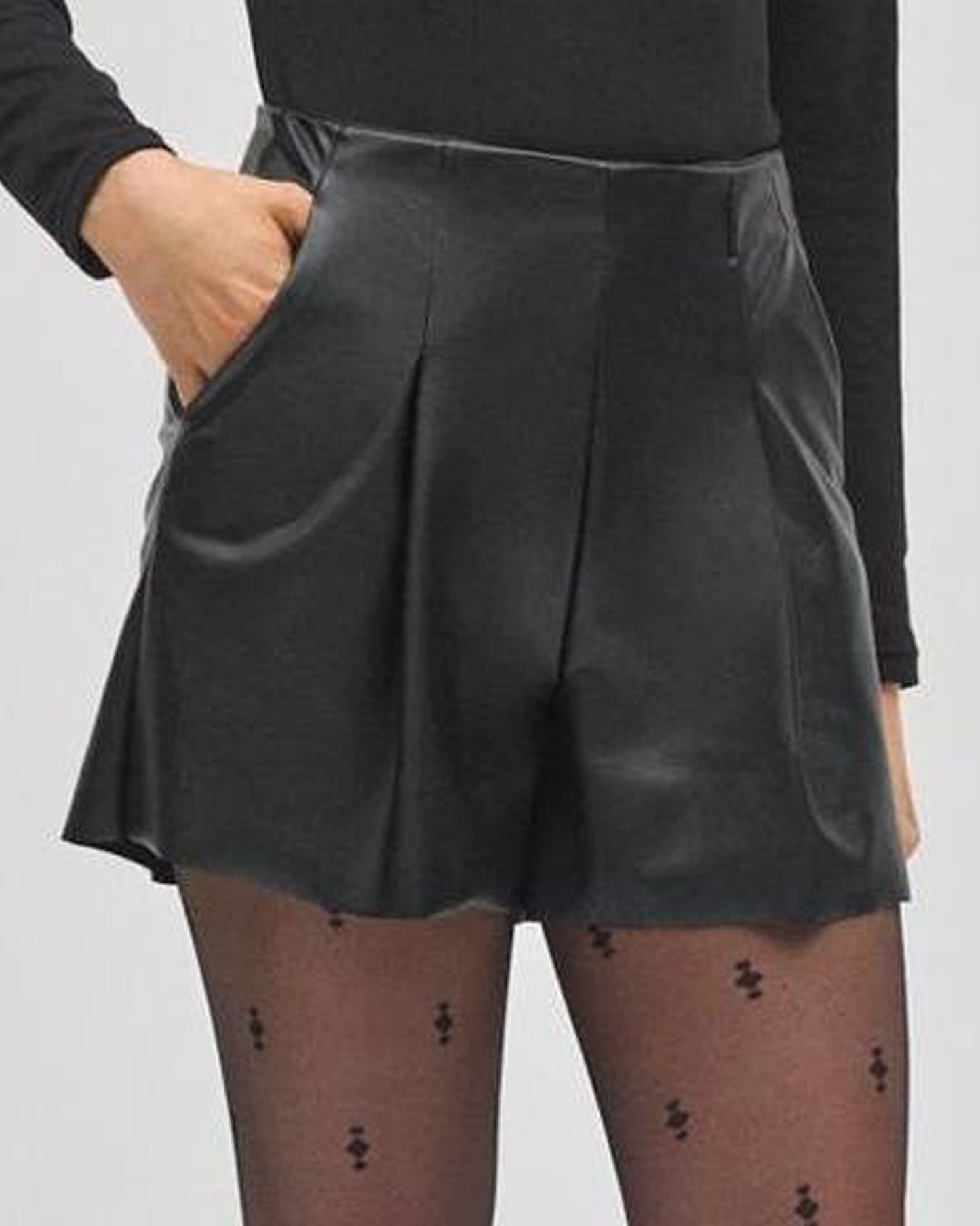 Person wearing a black pleated skort (skirt/shorts) with a plain background