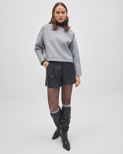 Woman wearing a gray sweater, black leather shorts, and gray knee-high socks, black boots on a white background