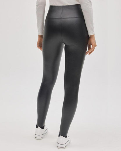 Black faux leather leggings worn with a white long sleeved top and white converse sneakers. Back view.