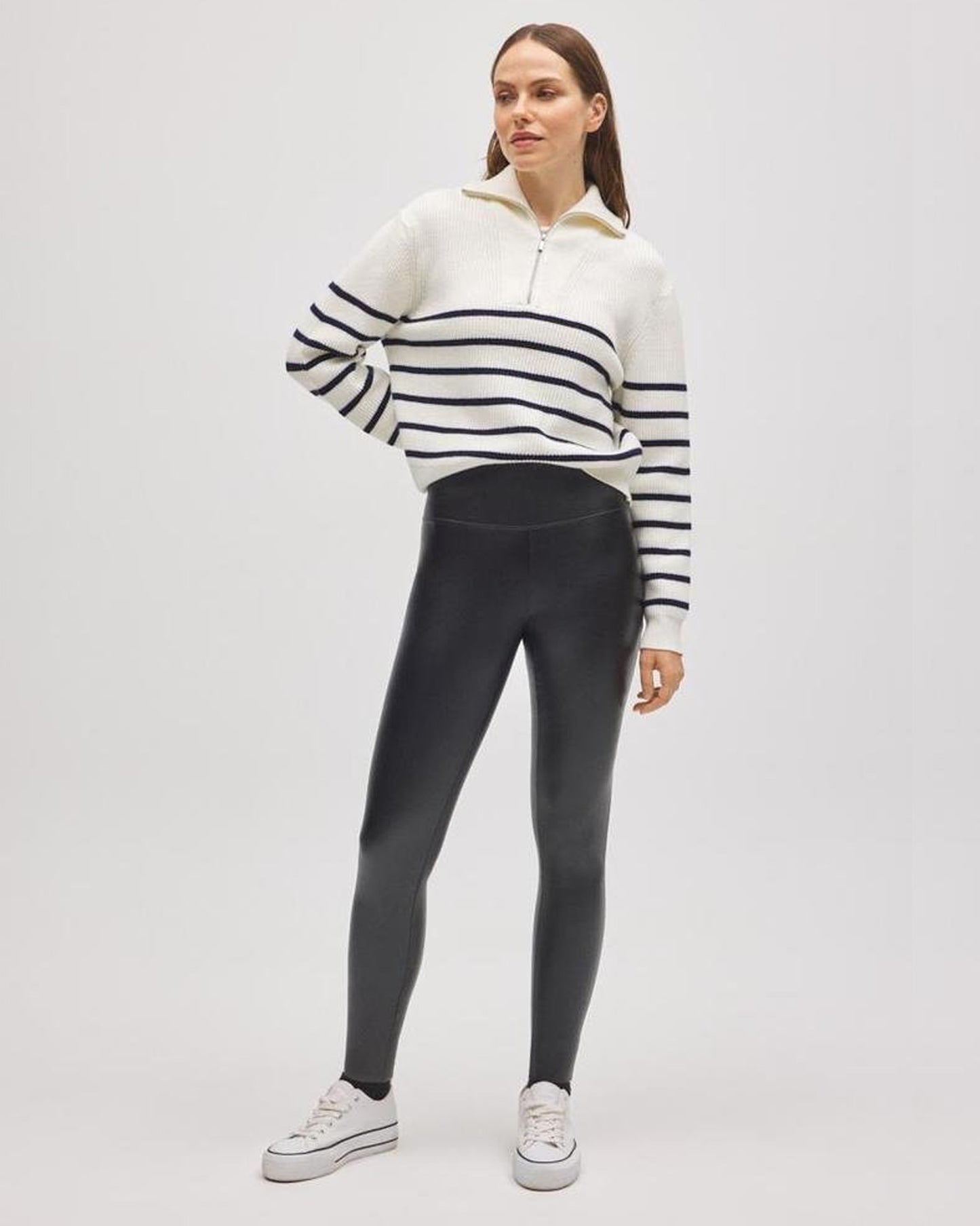 Woman wearing a striped half zip jumper and black faux leather leggings on a white background