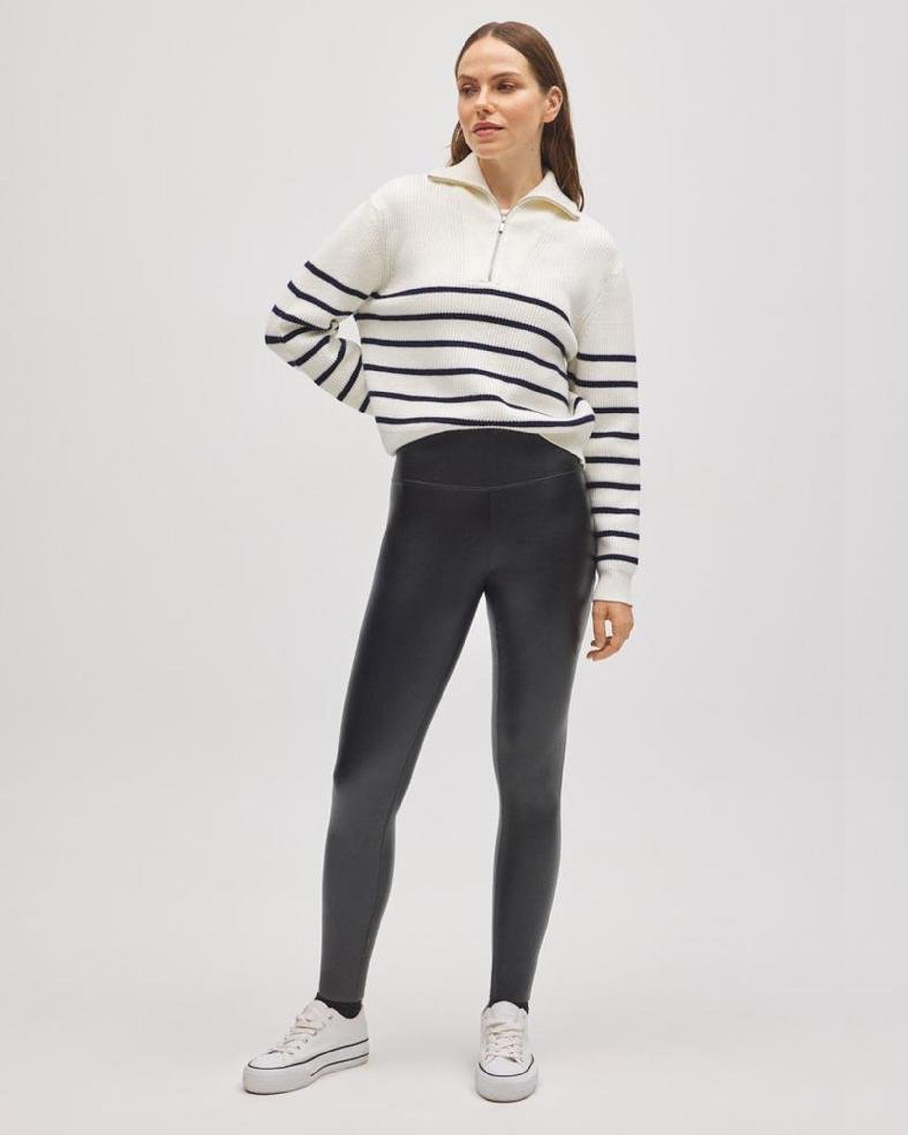 Woman wearing a striped half zip jumper and black faux leather leggings on a white background