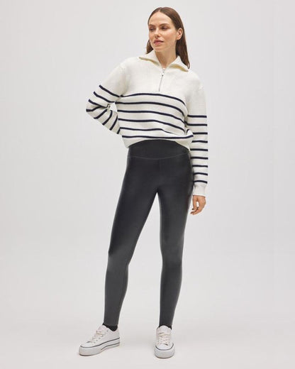 Woman wearing a striped half zip jumper and black faux leather leggings on a white background